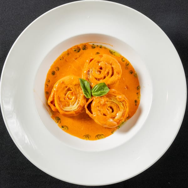 Three pasta rolls in a vibrant orange sauce, garnished with fresh basil leaves, on a white plate.