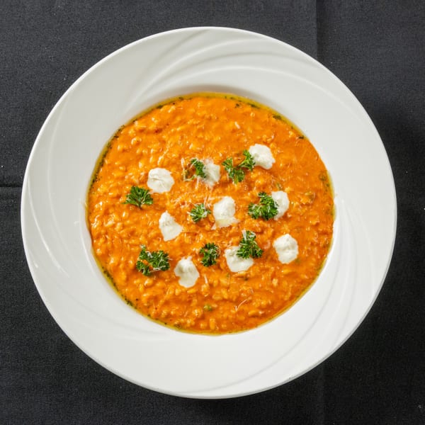 Vibrant orange risotto in a white bowl, garnished with dollops of cream, parsley, and grated cheese.