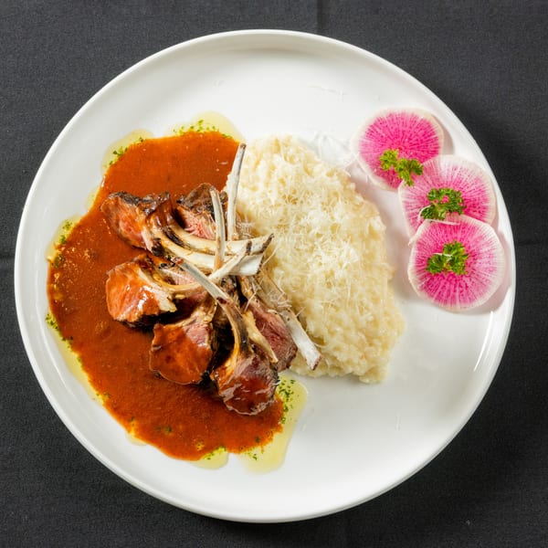 Lamb chops with red sauce, risotto, and watermelon radish slices on a white plate.
