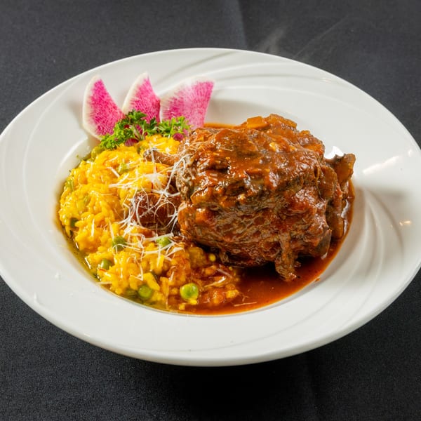 Braised short rib with saffron risotto, peas, parmesan, parsley, and watermelon radish on a white plate.