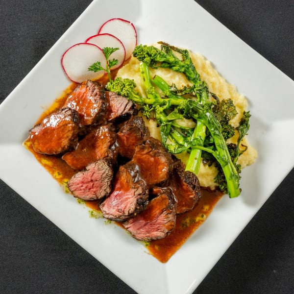 Plated steak medallions with red sauce, mashed potatoes, broccolini, and radish slices.