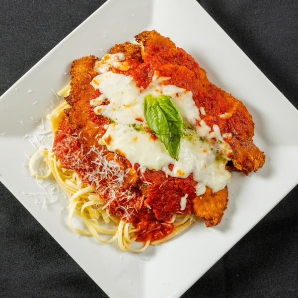 Chicken Parmesan with melted mozzarella, marinara sauce, fresh basil, and grated cheese over pasta.
