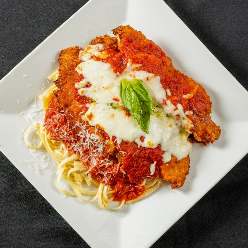 Chicken Parmesan with melted mozzarella, marinara sauce, fresh basil, and grated cheese over pasta.