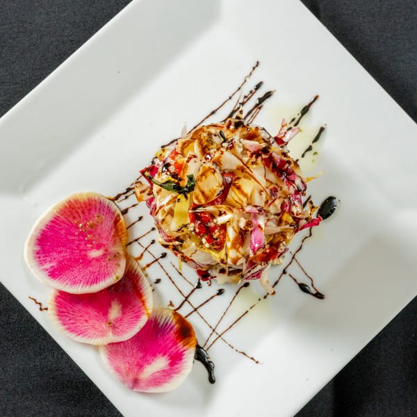 Gourmet salad with radicchio, vegetables, balsamic glaze, and watermelon radish slices on a white plate.