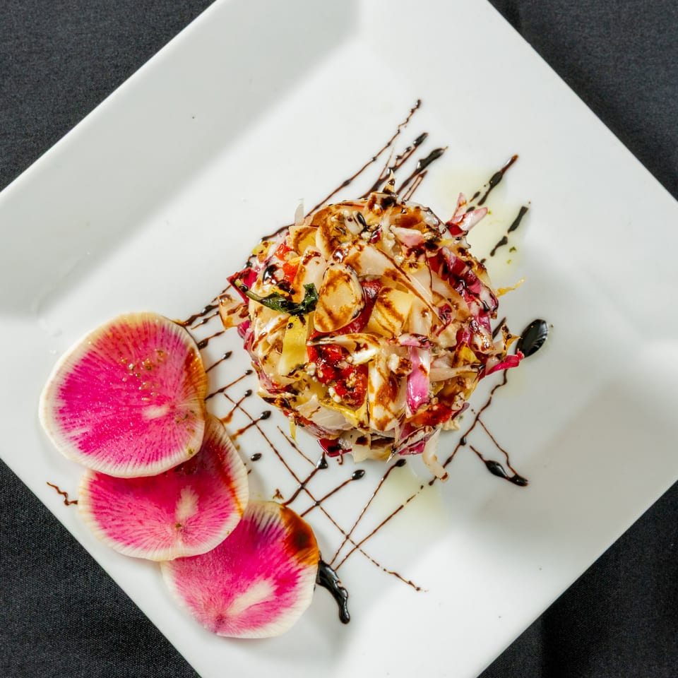 Gourmet salad with radicchio, vegetables, balsamic glaze, and watermelon radish slices on a white plate.