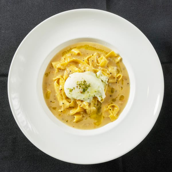 Creamy pasta dish with a poached egg and herbs, served in a white bowl on a dark tablecloth.