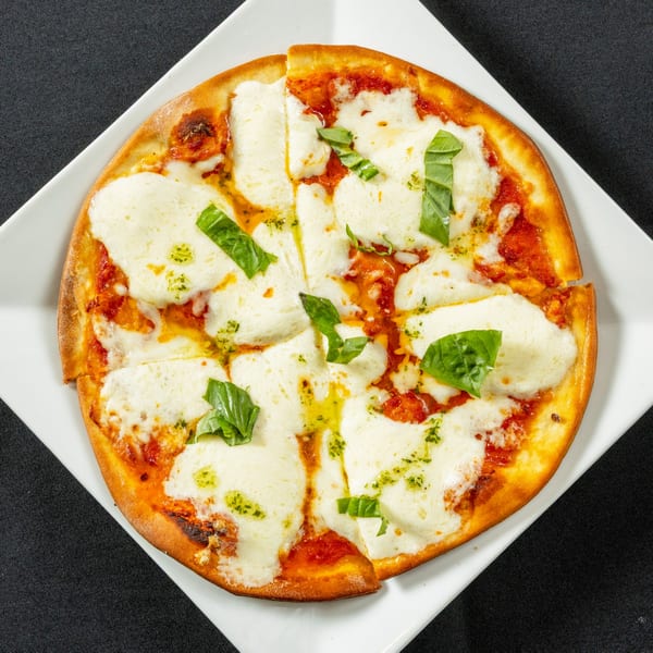 A round Margherita pizza with fresh mozzarella, tomato sauce, basil, and olive oil on a white plate.