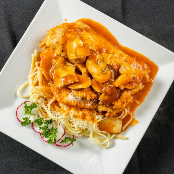 Chicken with mushroom sauce over spaghetti, garnished with radishes and parsley on a white plate.