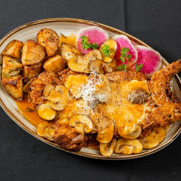 Breaded chicken cutlet with melted cheese, mushrooms, roasted potatoes, and watermelon radishes on a platter.
