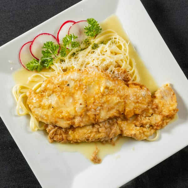 Chicken piccata with spaghetti, parmesan cheese, parsley, and radish slices on a white plate.