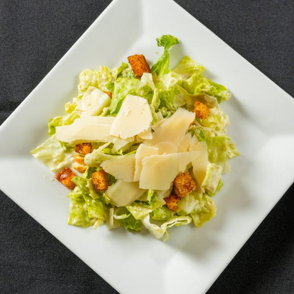 Caesar salad with romaine lettuce, croutons, and shaved Parmesan cheese on a white square plate.