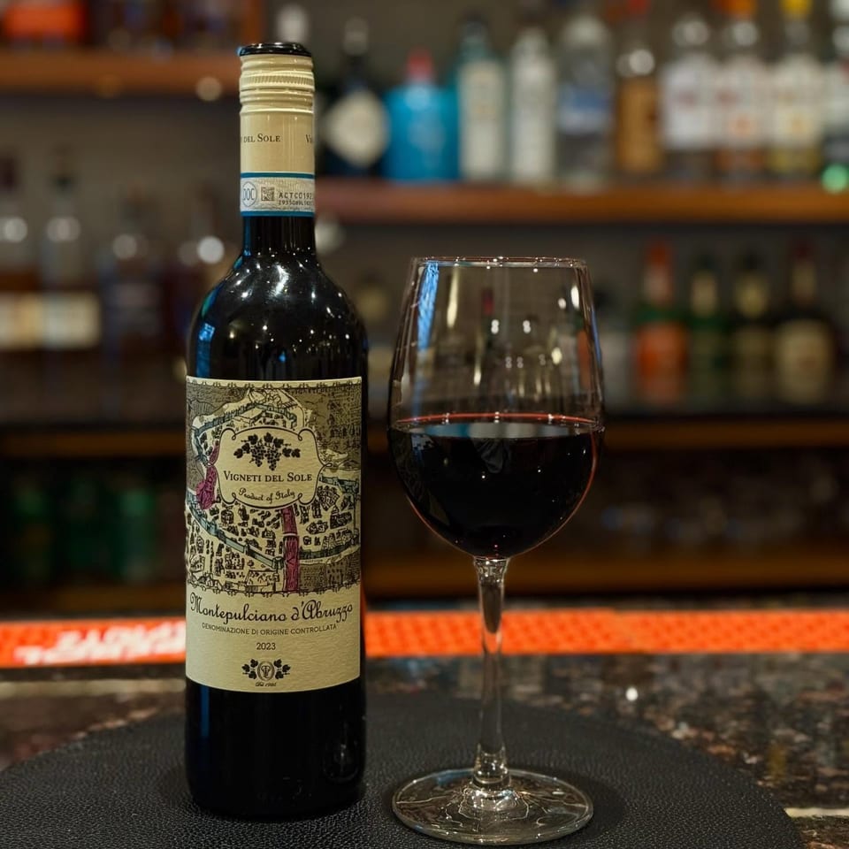A bottle of Vigneti del Sole Montepulciano d'Abruzzo wine next to a glass of red wine at a bar.